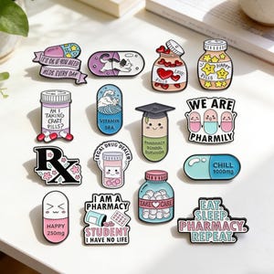 May include: A selection of enamel pins with pharmacy-related themes. The pins display pills, pill bottles, and text such as "Happy 250mg", "Chill 1000mg", and "Eat. Sleep. Pharmacy. Repeat."