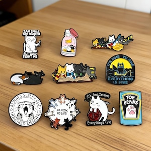 Pode incluir: Uma coleção de alfinetes de esmalte coloridos com designs de gatos. Os alfinetes incluem frases como "I am small and sensitive but also fight me", "Always Sleepy Club" e "Everything is Fine". Outros alfinetes retratam gatos em várias poses.