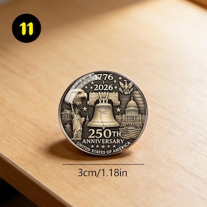 May include: A round, silver-colored commemorative coin with the text "1776-2026" and "250th Anniversary United States of America." The coin features the Liberty Bell, an eagle, the Statue of Liberty, and the Capitol building. The coin is 1.18 inches in diameter.