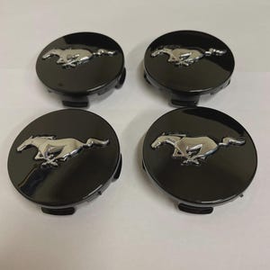 May include: Four black wheel center caps with a chrome running horse emblem. The caps are round and have a glossy finish. The running horse is a prominent, detailed design.
