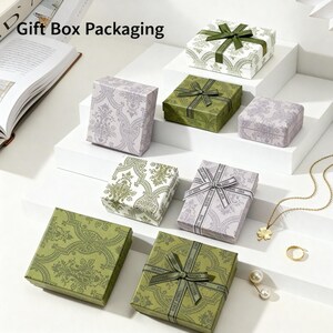 May include: Several decorative gift boxes in various sizes and colors, including green, white, and lavender. The boxes are adorned with patterned designs and ribbons. The text "Gift Box Packaging" is at the top.