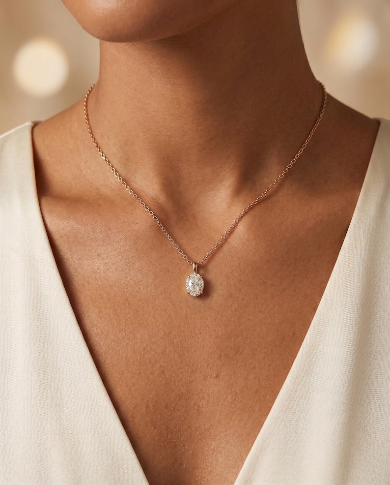 May include: A gold-coloured necklace with an oval pendant set with small, sparkling stones. The necklace is worn against a white garment, creating a contrast that highlights the jewellery.
