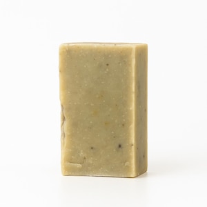 May include: A rectangular bar of soap with a light green hue and speckled texture. The soap has a slightly uneven surface and is set against a white background. The soap appears to be handmade.