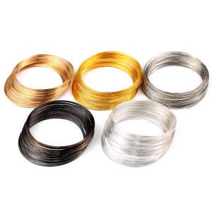 May include: Five circular coils of craft wire arranged in a group. The set includes one coil of copper-toned wire, one bright gold-toned coil, one dark gunmetal grey coil, one silver-toned coil, and one lighter, polished silver-toned wire coil.