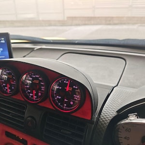 May include: Dashboard with three circular gauges with red lighting. The gauges are set in a black housing with red accents. A digital screen is visible to the left, displaying a time of 13:48. The dashboard is in a vehicle.