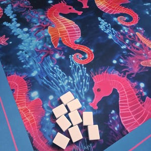 May include: A blue and pink play mat featuring a vibrant underwater scene with seahorses, coral, and the text "Beachy Maby". The mat has a blue border with a pink stripe and includes several white game tiles.