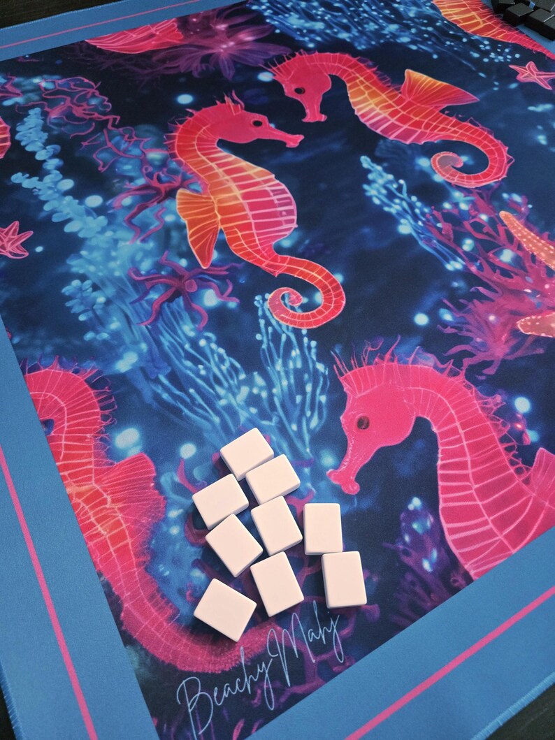 May include: A blue and pink play mat featuring a vibrant underwater scene with seahorses, coral, and the text "Beachy Maby". The mat has a blue border with a pink stripe and includes several white game tiles.