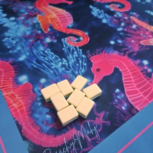 May include: A colorful game mat featuring a vibrant underwater scene with seahorses and coral in shades of pink, orange, and blue. The mat has the text "Beachy Mahj" and includes several cream-colored game tiles.