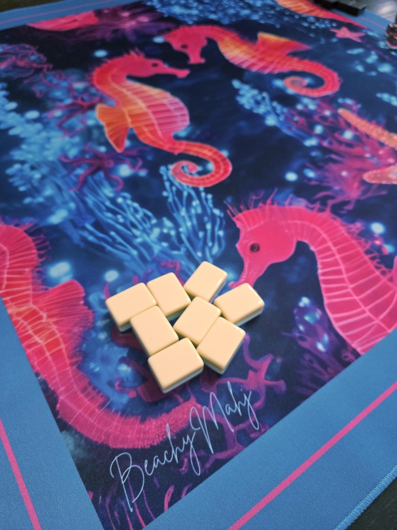 May include: A colorful game mat featuring a vibrant underwater scene with seahorses and coral in shades of pink, orange, and blue. The mat has the text "Beachy Mahj" and includes several cream-colored game tiles.