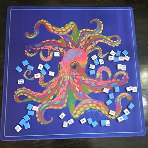 May include: A blue game mat featuring a colorful octopus illustration with rainbow hues. Scattered around the octopus are small, rectangular tiles with various symbols, suggesting a game like Mahjong. The mat has a teal border.