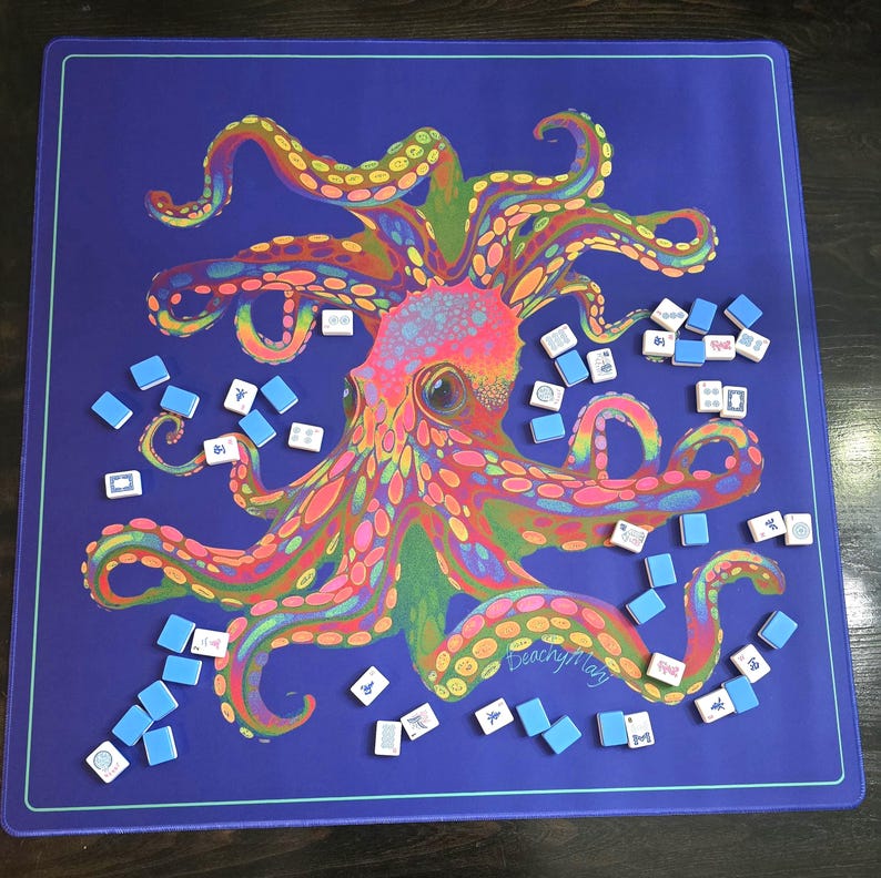 May include: A blue game mat featuring a colorful octopus illustration with rainbow hues. Scattered around the octopus are small, rectangular tiles with various symbols, suggesting a game like Mahjong. The mat has a teal border.