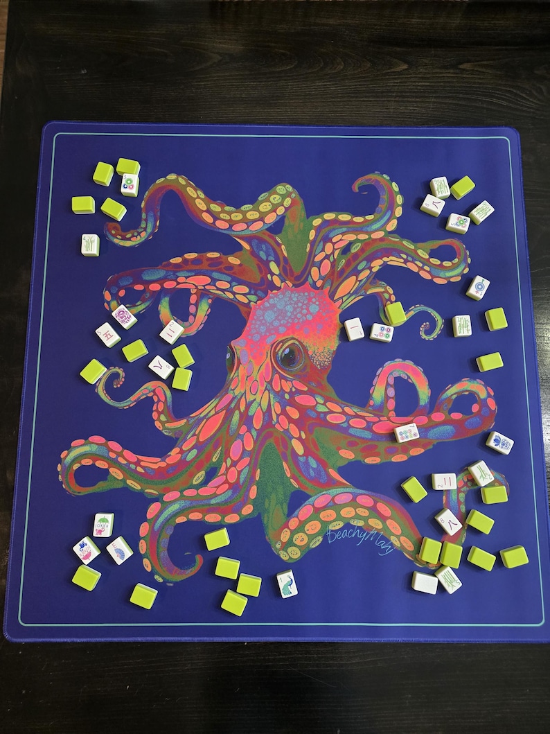 May include: A blue game mat featuring a colorful octopus design with a variety of game tiles scattered around it. The octopus is rendered in shades of pink, orange, green, and yellow. The mat has a light blue border and the text "peachy mary" is visible.