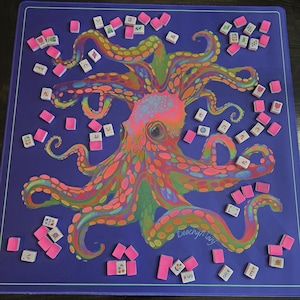 May include: A purple game mat featuring a colorful octopus illustration with pink, orange, and green accents. Scattered around the mat are pink tiles and white tiles with symbols. The mat has a thin purple border.