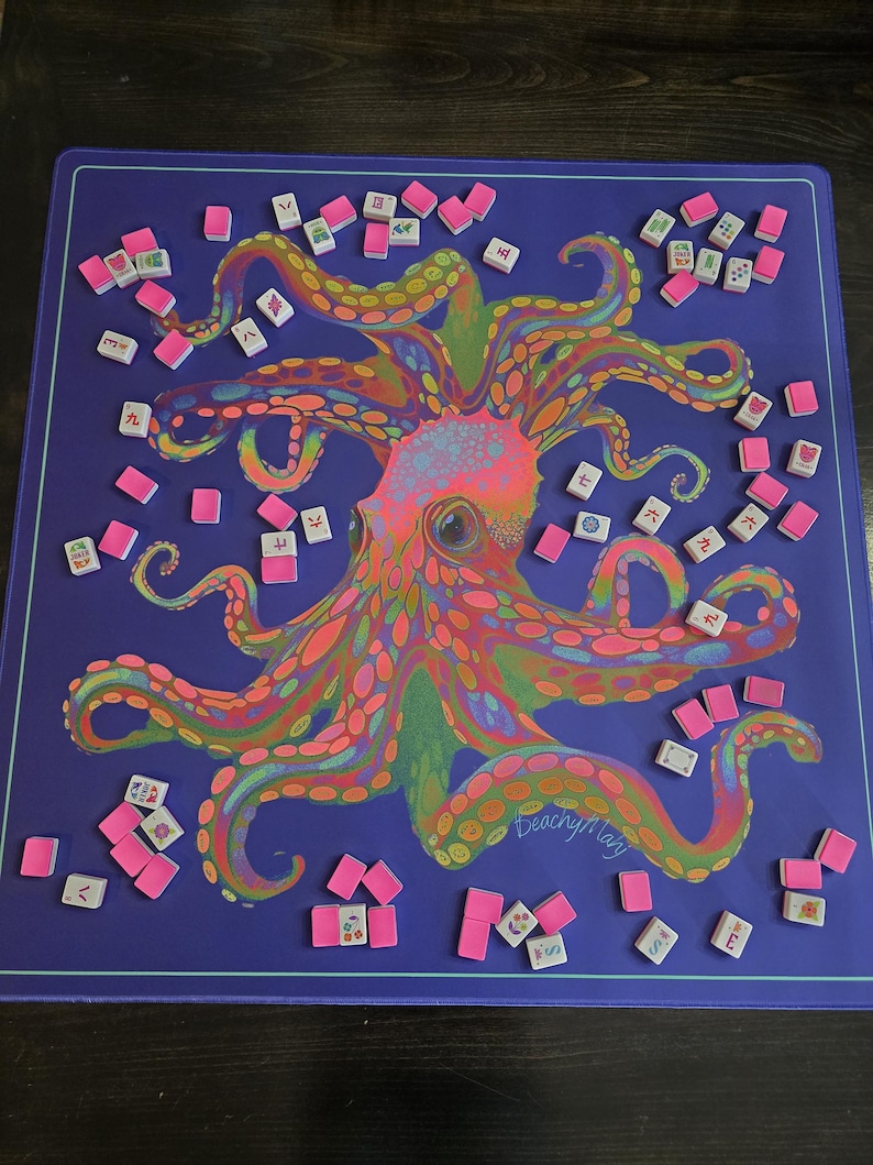 May include: A purple game mat featuring a colorful octopus illustration with pink, orange, and green accents. Scattered around the mat are pink tiles and white tiles with symbols. The mat has a thin purple border.