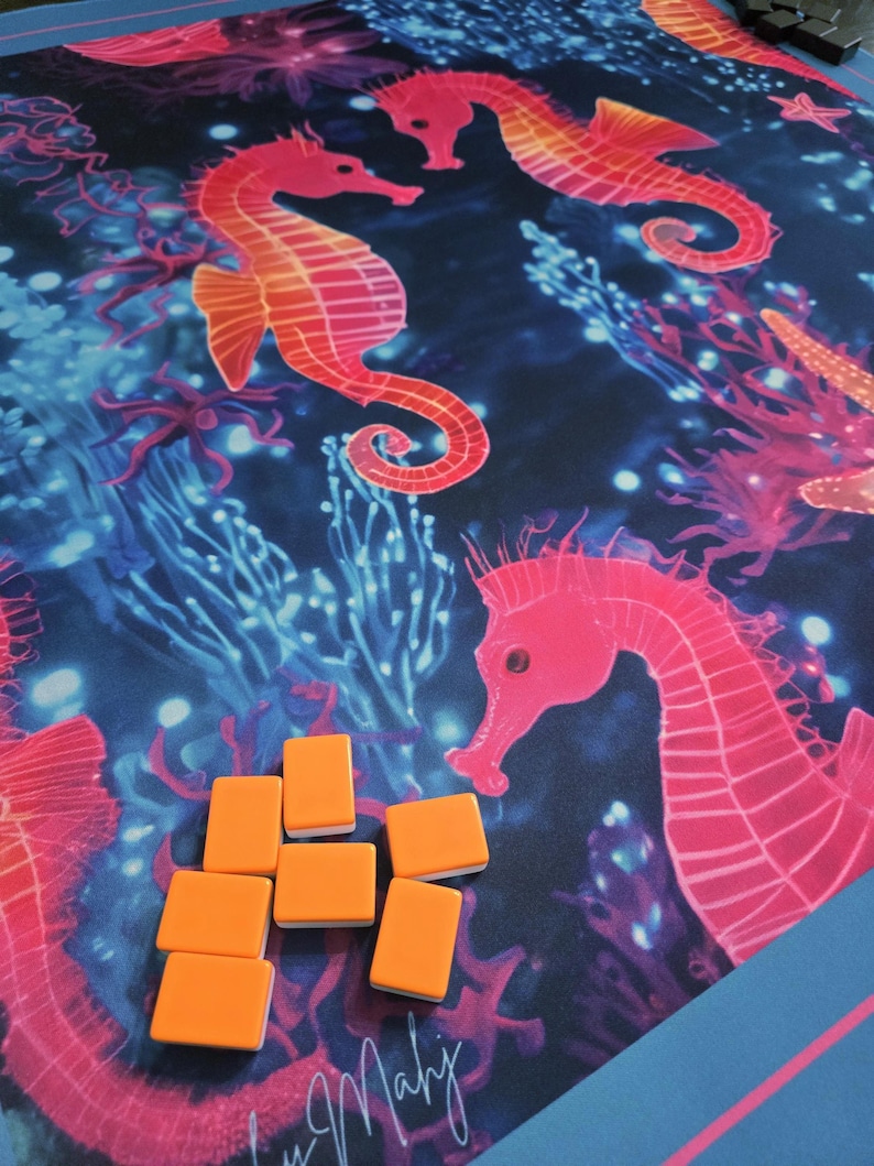 May include: A vibrant, marine-themed game mat featuring coral, seahorses, and other sea life in shades of pink, orange, and blue. Includes a set of orange game tiles. The mat has a blue border and a signature in the corner.