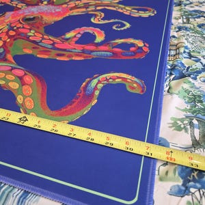 May include: A rectangular blue mat with a colorful octopus design. The octopus is depicted in shades of red, orange, green, and pink. The mat is approximately 31 inches long, measured with a yellow tape measure.