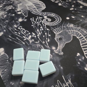 May include: Light blue square tiles arranged on a black and white seahorse patterned fabric. The fabric features a repeating design of seahorses and aquatic plants. The tiles are smooth and have a glossy finish.