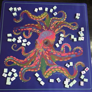 May include: A vibrant blue game mat featuring a colorful octopus illustration with pink, orange, green, and yellow details. Scattered around the mat are numerous white and green game tiles, suggesting a game of Mahjong.