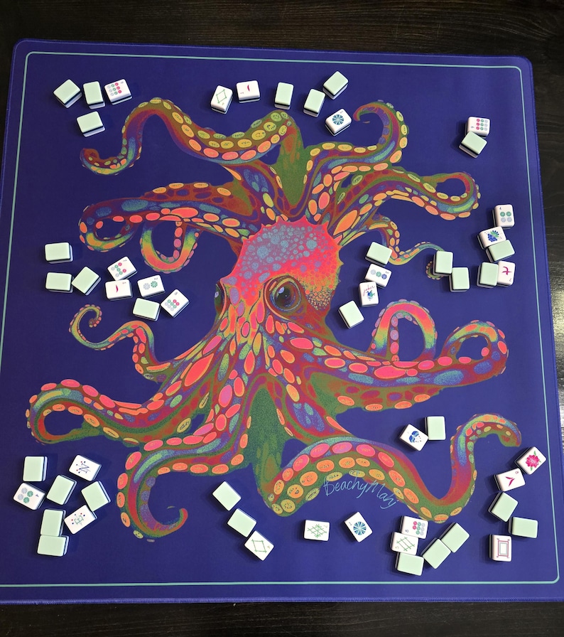 May include: A vibrant blue game mat featuring a colorful octopus illustration with pink, orange, green, and yellow details. Scattered around the mat are numerous white and green game tiles, suggesting a game of Mahjong.