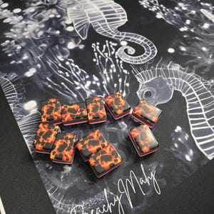 May include: A collection of rectangular game pieces with a tortoiseshell pattern in shades of orange, red, and black. They are arranged on a black surface with a white seahorse design and the text "Beachy Mahj".
