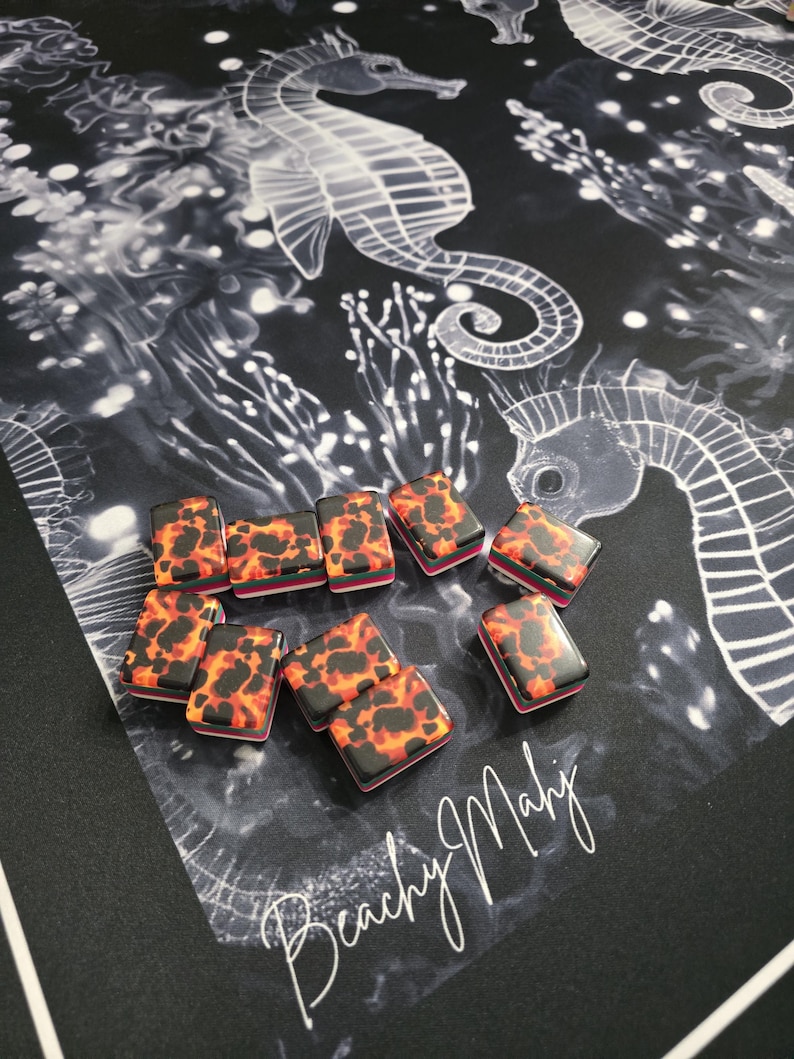 May include: A collection of rectangular game pieces with a tortoiseshell pattern in shades of orange, red, and black. They are arranged on a black surface with a white seahorse design and the text "Beachy Mahj".