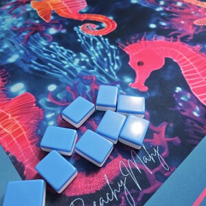 May include: A blue and white tile game with a marine-themed background featuring seahorses and coral. The background is a vibrant mix of blue, pink, and orange. The tiles are light blue with white edges, and the text "Beachy Mary" is visible.