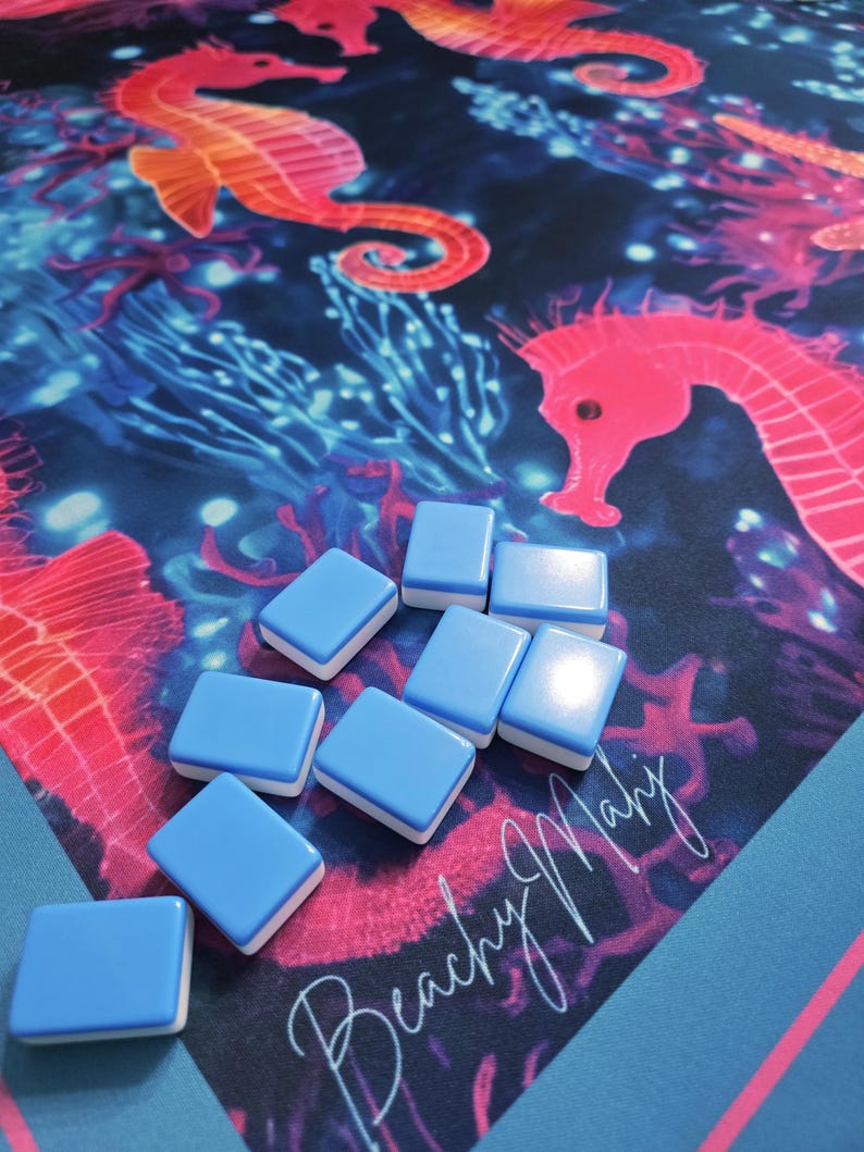 May include: A blue and white tile game with a marine-themed background featuring seahorses and coral. The background is a vibrant mix of blue, pink, and orange. The tiles are light blue with white edges, and the text "Beachy Mary" is visible.