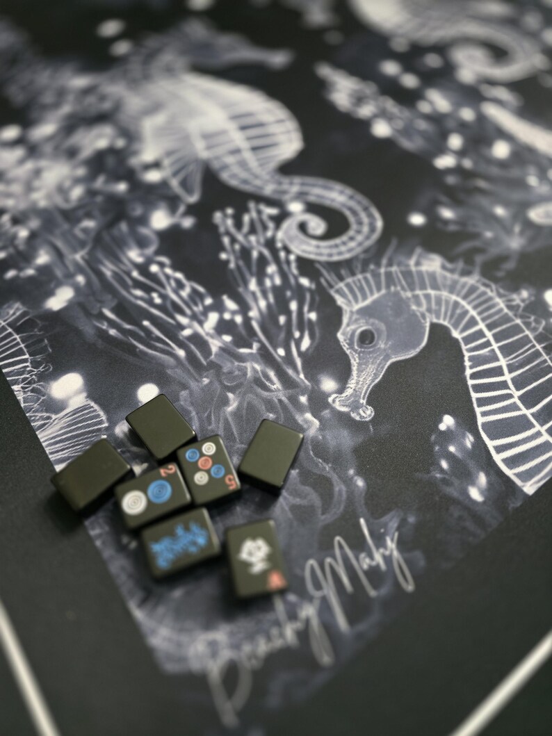 May include: A collection of black Mahjong tiles with colorful symbols and numbers, resting on a dark background with a seahorse and coral design. The design is in white and the tiles are rectangular.