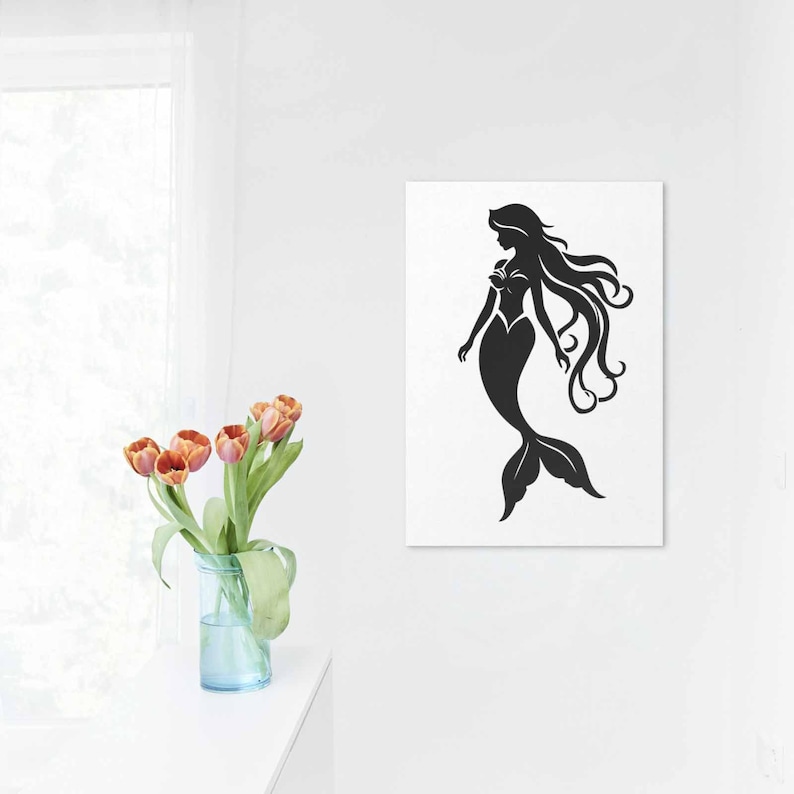 May include: Black silhouette of a mermaid on a white background. The mermaid has long flowing hair and a fishtail. The artwork is displayed on a white wall, with a vase of orange tulips in the foreground.