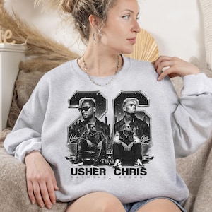 A black and white digital art piece featuring portraits of singers Usher and Chris Brown sitting in front of a stylized city skyline with the text "USHER x CHRIS" and decorative "22" branding elements.
