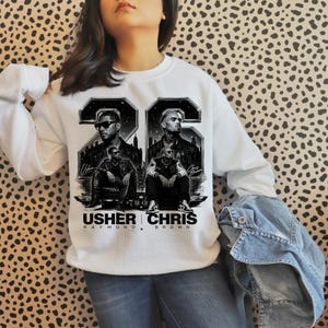 A black and white digital art piece featuring portraits of singers Usher and Chris Brown sitting in front of a stylized city skyline with the text "USHER x CHRIS" and decorative "22" branding elements.