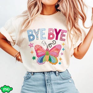 May include: Cream-colored t-shirt featuring the words "BYE BYE" in patchwork letters above a colorful butterfly design. The butterfly has patchwork wings and a rainbow body, surrounded by star accents. A whimsical and cheerful design.