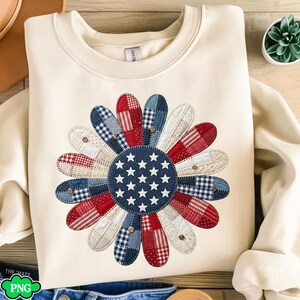 Peut inclure: Sweat-shirt crème avec un grand motif floral patriotique. Les pétales de la fleur sont faits de tissu patchwork aux motifs rouges, blancs et bleus, avec un centre bleu orné d'étoiles blanches. Le motif est centré sur le devant du sweat-shirt.
