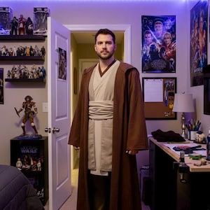 May include: A person wearing a brown Jedi robe with a light tan tunic and pants. The room has Star Wars posters and figurines on shelves. The lighting is provided by a strip of purple LED lights.