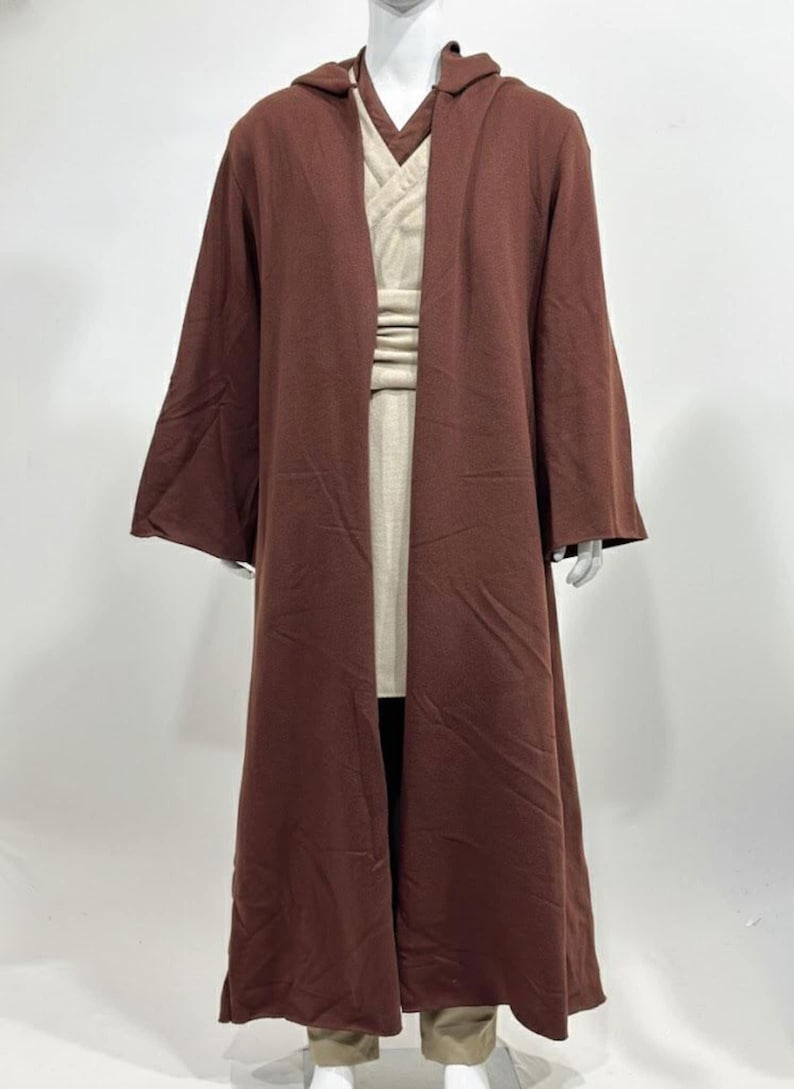 May include: A brown hooded robe with long sleeves, layered over a beige tunic and pants. The costume is displayed on a mannequin. The robe has a wide, flowing design, and the tunic has a V-neck. The outfit is a cosplay costume.