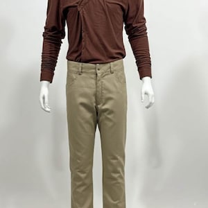 May include: A brown long-sleeve shirt with a V-neck design and tan pants. The shirt has a wrap-style closure. The pants are a neutral color and have a classic five-pocket design. The outfit is displayed on a mannequin.