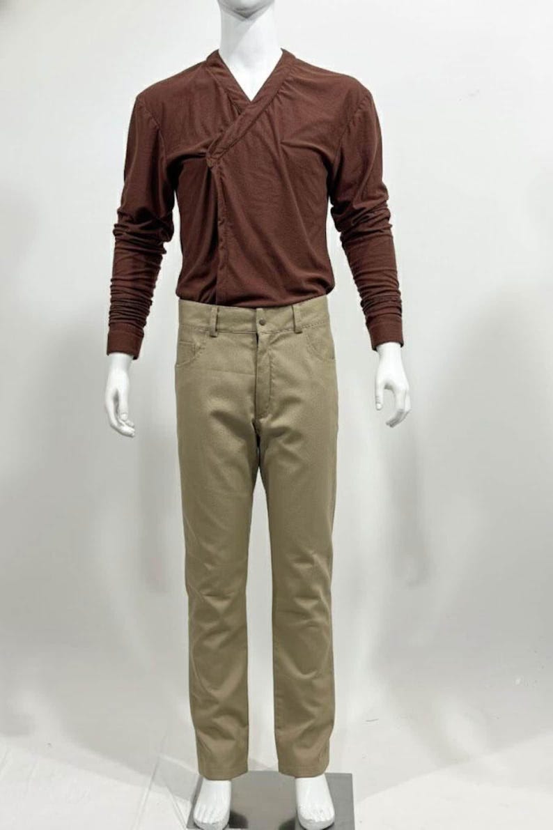 May include: A brown long-sleeve shirt with a V-neck design and tan pants. The shirt has a wrap-style closure. The pants are a neutral color and have a classic five-pocket design. The outfit is displayed on a mannequin.