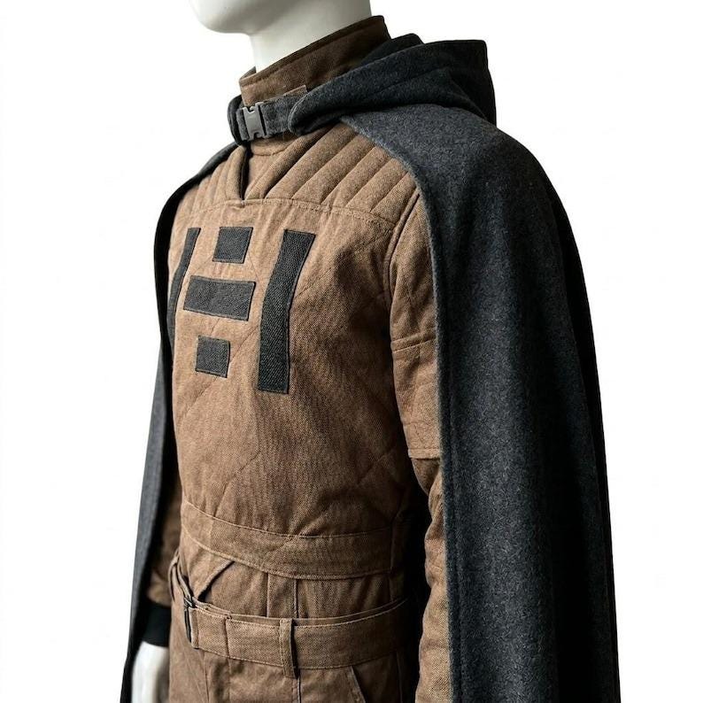 May include: A brown quilted jumpsuit with a dark gray hooded cape. The jumpsuit features a geometric design on the chest and a belt at the waist. The cape is attached at the shoulders and has a buckle closure at the neck. The outfit is designed for cosplay or costume use.