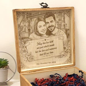 Può includere: Una scatola quadrata in legno per ricordi con coperchio incernierato, caratterizzata da un ritratto inciso al laser di una coppia e dal testo: May this box hold not just what's inside but the love and memories that fill our lives. Est. October 1st, 2024.