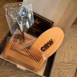 May include: A wooden beard grooming kit in a box. The kit includes a wooden comb, scissors, and a card that says "The best wishes to you". The comb has the letters "CRW" on it.