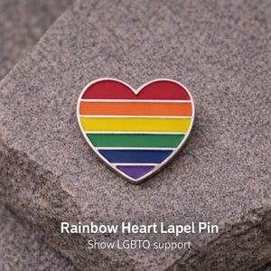 May include: A heart-shaped lapel pin with a rainbow design, featuring red, orange, yellow, green, blue, and purple stripes. The pin has a silver border and the text "Rainbow Heart Lapel Pin" and "Show LGBTQ support".