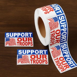 May include: A roll of white stickers with the text "SUPPORT OUR TROOPS" in red and blue, along with an American flag design. Two individual stickers are also visible, displaying the same message and design.