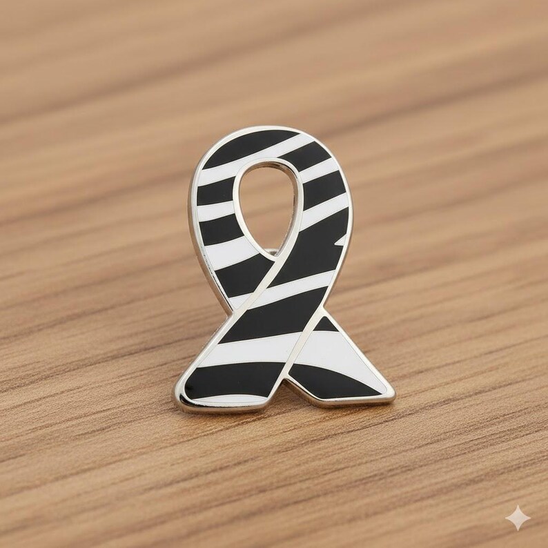 May include: A silver-toned ribbon pin with a black and white striped design. The pin is in the shape of a ribbon, with a polished finish. The pin is set against a wooden surface.