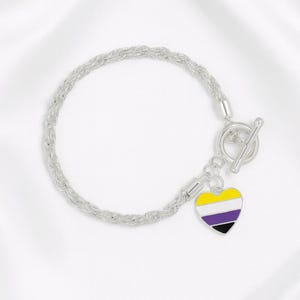 May include: Silver-toned bracelet with a toggle clasp. A heart-shaped charm with a yellow, white, purple, and black non-binary pride flag design hangs from the bracelet. The bracelet has a braided rope design.