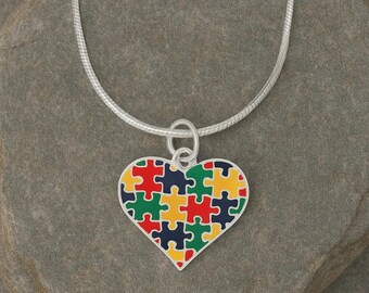 May include: A silver necklace with a heart-shaped pendant. The pendant is made of puzzle pieces in red, yellow, green, and blue. The necklace is on a silver chain.