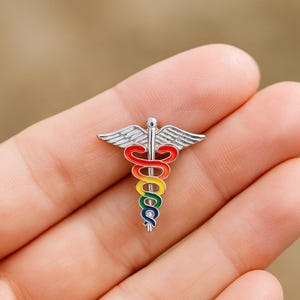 Peut inclure: &Eacute;pingle Caduc&eacute;e argent&eacute;e avec un serpent et des ailes aux couleurs de l'arc-en-ciel. Ce symbole m&eacute;dical est un accessoire color&eacute;, id&eacute;al pour les professionnels de la sant&eacute;. L'&eacute;pingle est petite et d&eacute;taill&eacute;e, parfaite pour une veste.