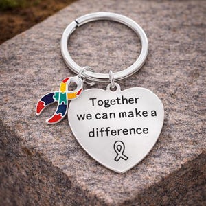 May include: A silver-colored keychain with a heart-shaped charm and a colorful ribbon pendant. The heart charm has the words "Together we can make a difference" engraved on it. The ribbon is in the colors of the autism awareness symbol.