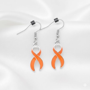 May include: A pair of silver-toned earrings featuring orange ribbon-shaped charms. The earrings have a hook design for pierced ears and are set against a white, textured background.