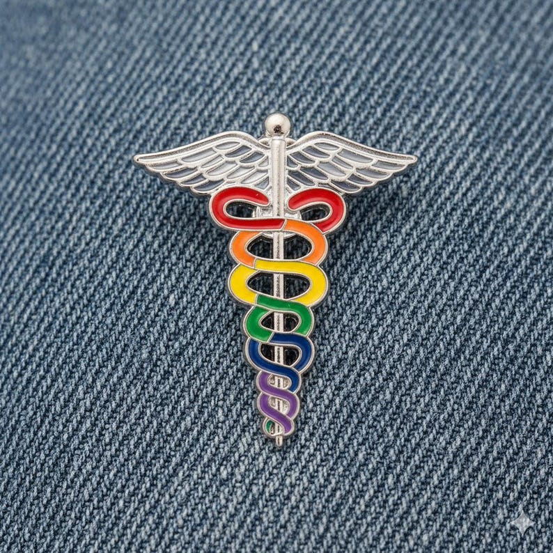 Peut inclure: &Eacute;pinglette en m&eacute;tal argent&eacute; repr&eacute;sentant le symbole du Caduc&eacute;e, avec un serpent aux couleurs de l'arc-en-ciel enroul&eacute; autour d'un b&acirc;ton et des ailes. L'&eacute;pinglette est pos&eacute;e sur un fond en denim bleu.