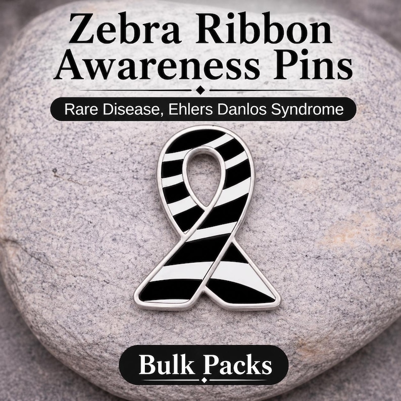 May include: A zebra ribbon awareness pin with black and white stripes, set against a gray stone background. The pin is for rare disease and Ehlers Danlos Syndrome awareness. Text on the image reads "Zebra Ribbon Awareness Pins", "Rare Disease, Ehlers Danlos Syndrome", and "Bulk Packs".